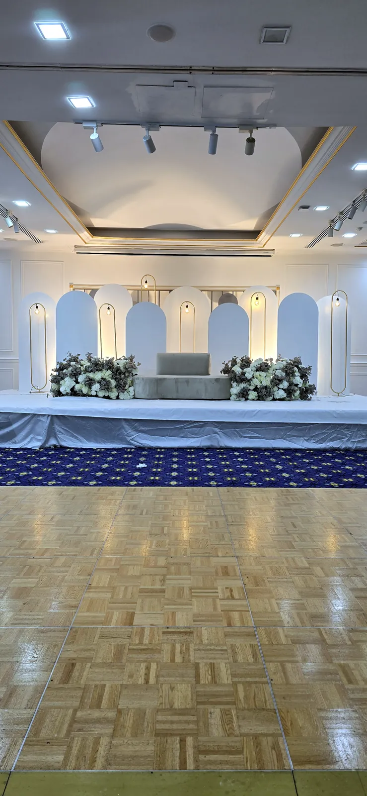 Ballroom stage with a white arcade, flowers and a blue carpet