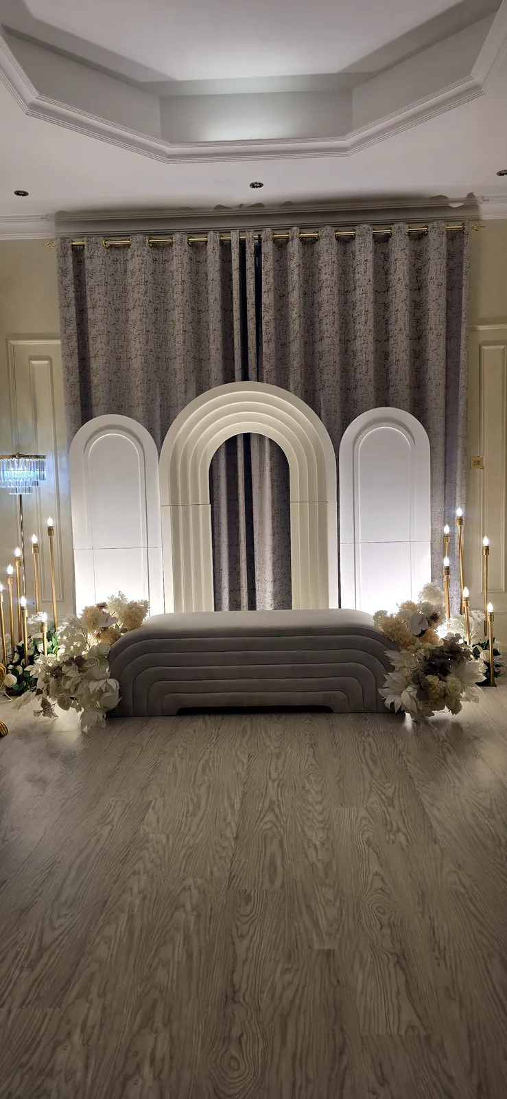 Layered arch backdrop with a sofa and white flowers on a wooden floor