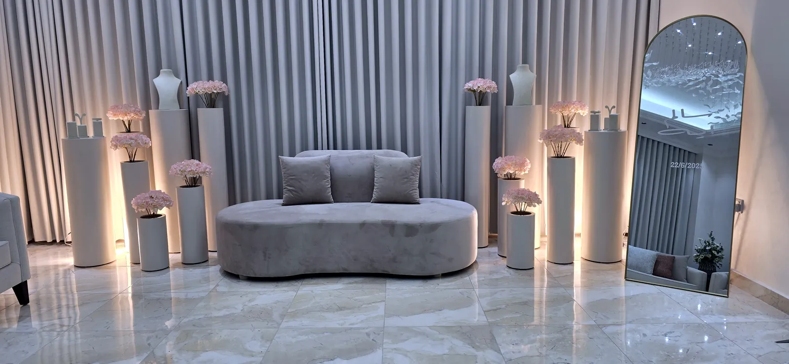 Grey sofa between white pillars with flowers and an arched mirror