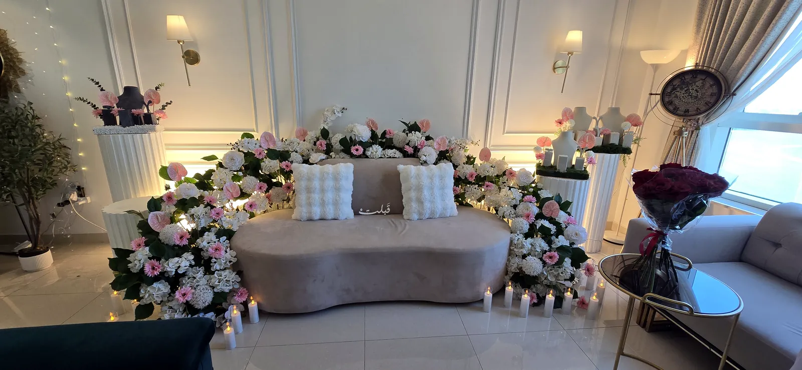 Sofa with white cushions surrounded by blush roses in a bright lounge
