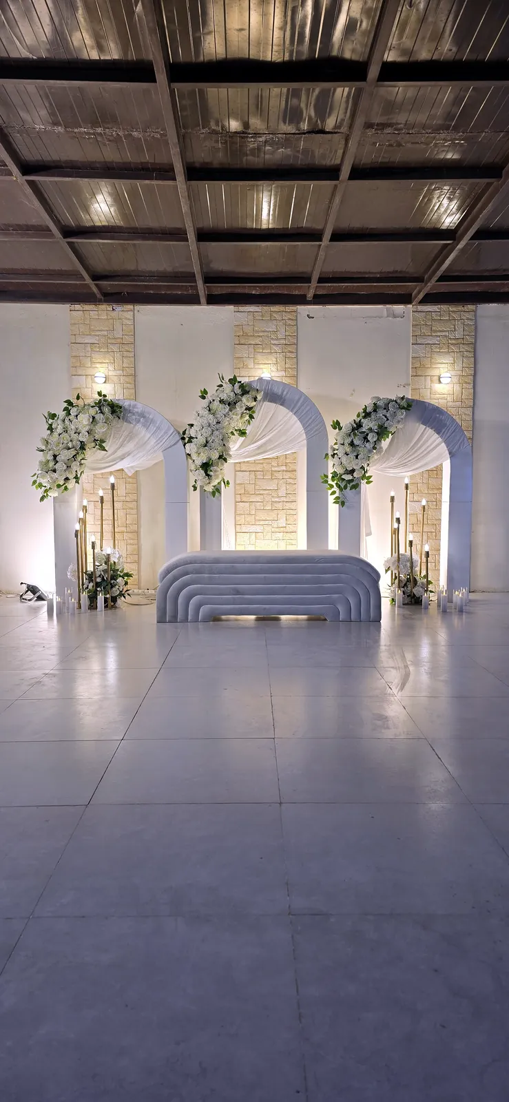Three white arches with flowers behind a stage sofa in a large hall