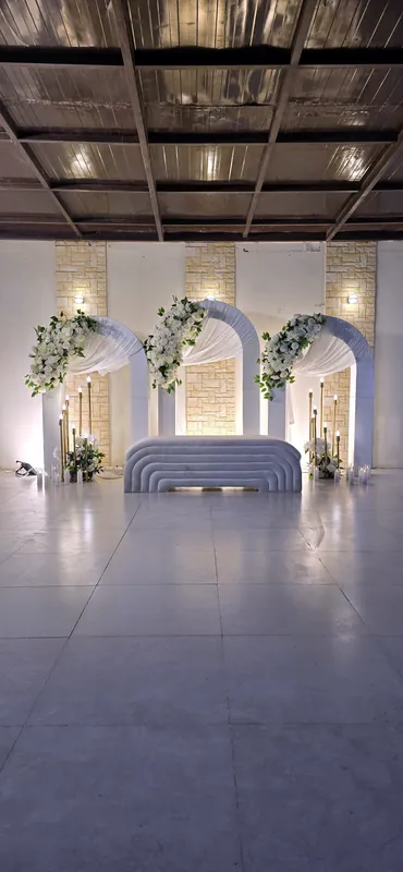 Three white arches with flowers behind a stage sofa in a large hall