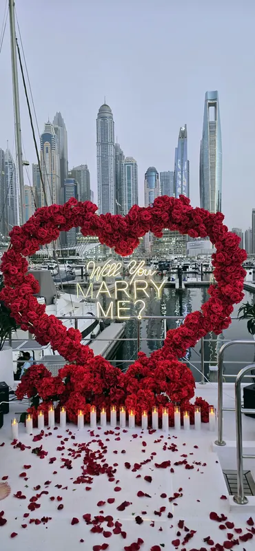 Red rose heart with a marry me sign on a yacht deck with marina towers behind