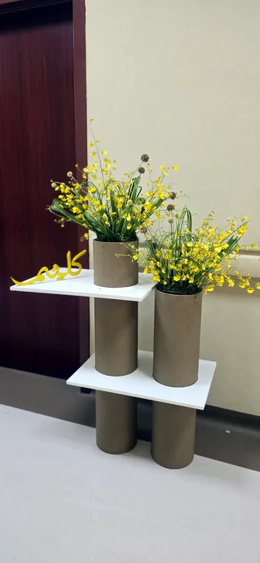 Yellow flowers on round taupe stands against a white wall